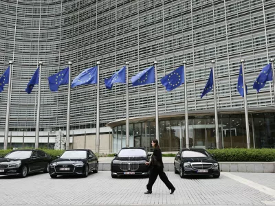 European Union flags flap in the wind as a woman walks past diplomatic vehicles outside of EU headquarters in Brussels, Belgium, Tuesday, May 27, 2025. (AP Photo/Omar Havana)