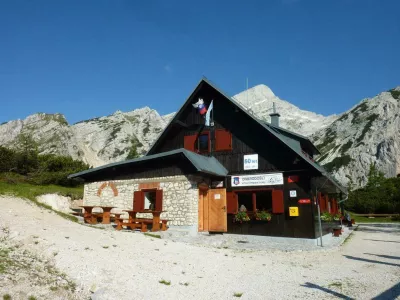 Poštarski dom na Vršiču ima med vsemi vršiškimi postojankami najlepši razgled; na vzpetini pred domom je razgledna plošča z označenimi vrhovi, ki se vidijo. F Kranjska gora