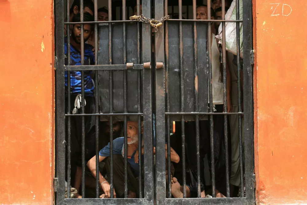 Prisoners stand behind a door, locked up with a pair of handcuffs, inside Malir Jail, after dozens of prisoners escaped from the jail, on the outskirts of Karachi, Pakistan, June 3, 2025. REUTERS/Akhtar Soomro