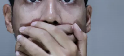 frightened asian man covering his mouth with both hands, expressing surprise, fear, or disbelief on grey blurry background / Foto: Muhammad Faris