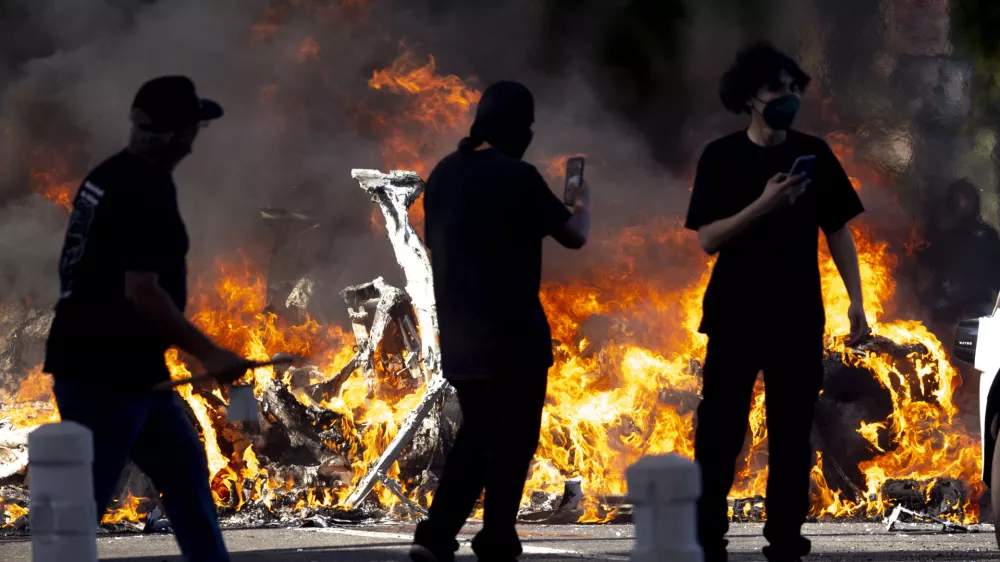 08 June 2025, US, Los AngelesProtesters walk by one of several Waymo cars that were set on fire in Downtown LA where hundreds gathered to protest immigration sweeps. PhotoJill Connelly/ZUMA Press Wire/dpa