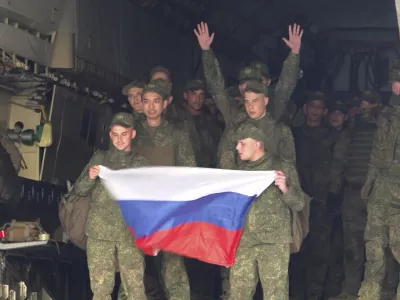 In this photo, taken from video and released by Russian Defense Ministry Press Service on Monday, June 9, 2025, Russian servicemen hold a Russian national flag as they leave a plane after returning from captivity by a POWs exchange of the first group of servicemen under 25 years of age between Russia and Ukraine, at an airport outside Moscow, Russia. (Russian Defense Ministry Press Service via AP)