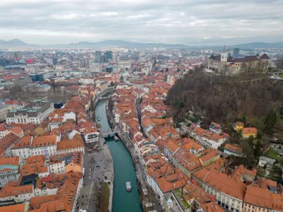 Panorama of Ljubljana city. Aerial view above Ljubljanica river with river cruise boats towards city center. Historical town with old architecture and the castle on the hill. Cloudy day in the winter. / Foto: Izvir8