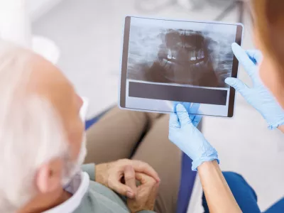 Dentist explaining necessary procedures to patient sitting in dental chair while looking at jaw x-ray at stomatology clinic / Foto: Vladans