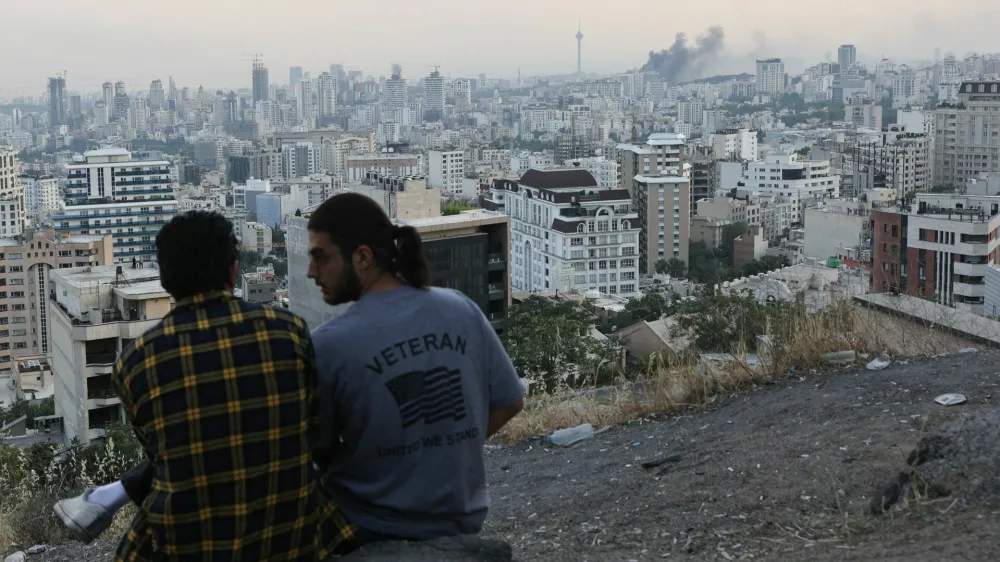A man wears a U.S. veteran-themed shirt, that reads, "United we stand", as smoke rises in the distance, following an Israeli attack on the IRIB building, the country's state broadcaster, in Tehran, Iran, June 16, 2025. Majid Asgaripour/WANA (West Asia News Agency) via REUTERS  ATTENTION EDITORS - THIS PICTURE WAS PROVIDED BY A THIRD PARTY. TPX IMAGES OF THE DAY.