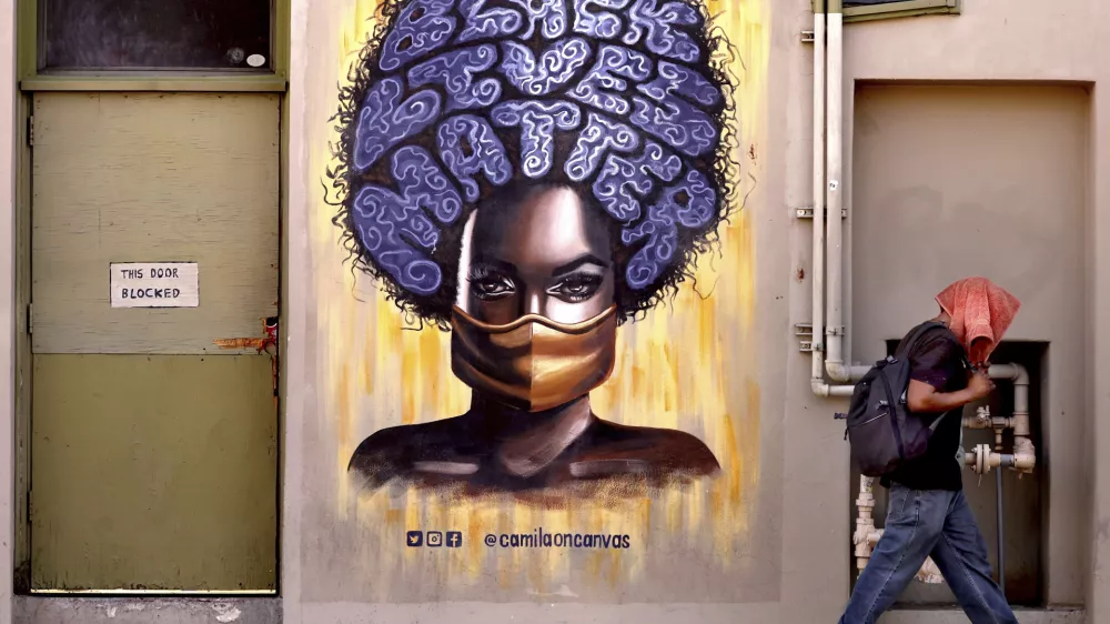 A pedestrian trying to beat the heat trudges by one of the murals on the walls of Hotel Congress as temperatures rise above 100 degrees Fahrenheit (38 degree Celsius) in Tucson, Ariz., on Juneteenth, Thursday, June 19, 2025. (Kelly Presnell/Arizona Daily Star via AP)