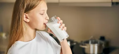 Side view of a blonde Caucasian teen taking a sip of milk from the glass / Foto: Yacobchuk