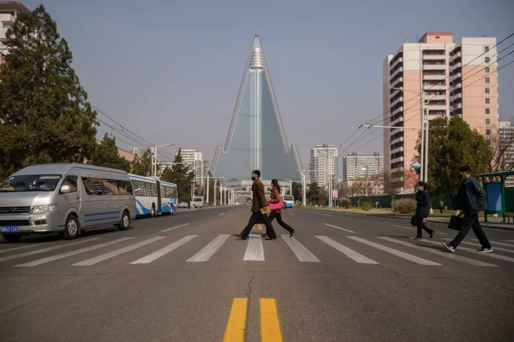 People wearing face masks walk across a street before the Ryugyong hotel (back C) on the occasion of the 108th birthday of late North Korean leader Kim Il Sung, known as the 'Day of the Sun', in Pyongyang on April 15, 2020.,Image: 513917283, License: Rights-managed, Restrictions:, Model Release: no