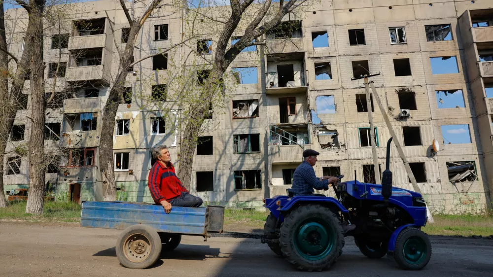 Men ride a mini tractor past a multi-storey residential building destroyed in the course of Russia-Ukraine conflict in Toshkivka (Toshkovka) in the Luhansk region, a Russian-controlled area of Ukraine, April 17, 2025. REUTERS/Alexander Ermochenko