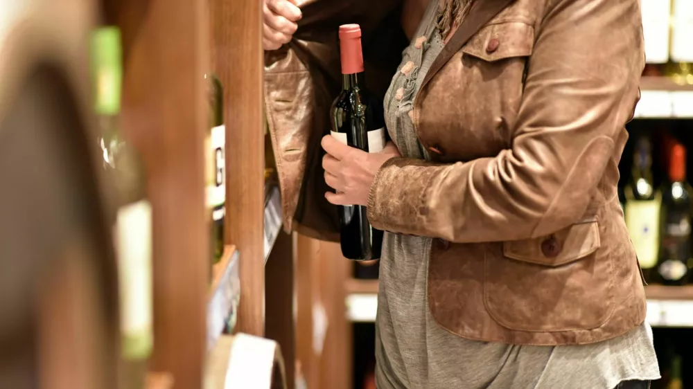 shoplifting - a woman steals a bottle of wine in a supermarket / Foto: Industryview