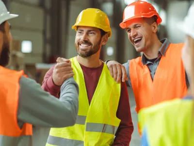 Attractive, happy, bearded, middle aged man wearing protective helmet shaking hands with colleagues standing in warehouse, greetings, deal. Concept of cooperation, communication / Foto: Mariia Vitkovska