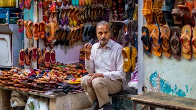 nathdwara, India – February 21, 2021: A shopkeeper sitting outside at his Juttis & Mojaris shop listening to something on the phone