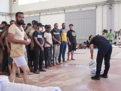 A Greek coast guard gives water to migrants from Africa as they take a shelter in Agia port, Chania, Crete island, Greece, Monday, July 7, 2025. (AP Photo/Giannis Angelakis)