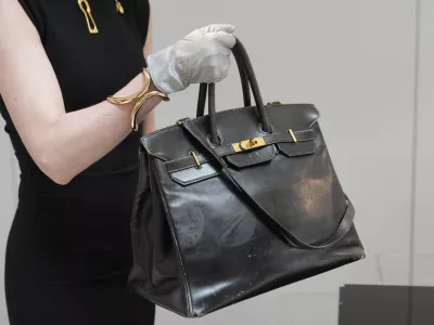 An auction officer carries the original Birkin bag created by Hermès for Jane Birkin in 1984, prior to its auction Thursday, July 10, 2025 in Paris. (AP Photo/Michel Euler)