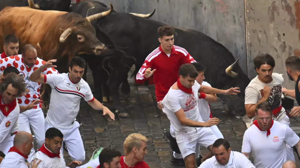 Revelers run alongside La Palmosilla's fighting bulls during the seventh running of the bulls at the San Fermín festival in Pamplona, Spain, Sunday, July 13, 2025. (AP Photo/Miguel Oses)