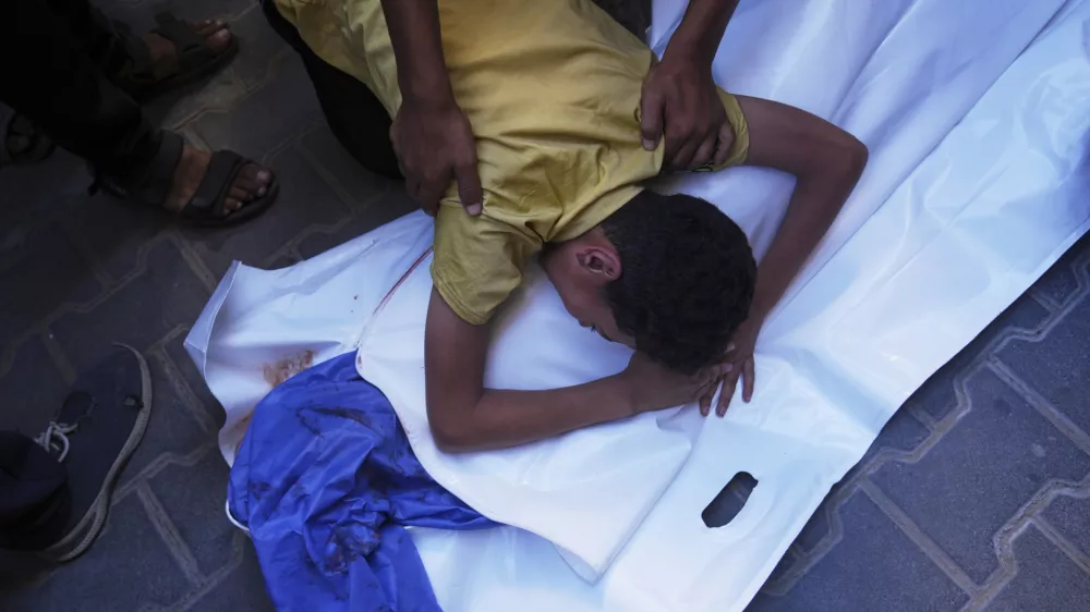 A Palestinian boy mourns over the body of his 12-year-old friend, Abdullah Ahmed, who was killed in an Israeli strike that targeted a drinking water distribution point, at Al-Awda Hospital in Nuseirat, central Gaza Strip, Sunday, July 13, 2025. (AP Photo/Abdel Kareem Hana)