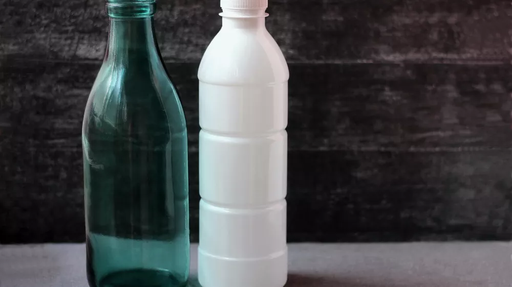 Glass milk bottle and plastic white bottle on grey background. Reusable packaging. The concept of environmental protection.Empty space for text. Selective focus.