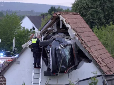 A police officer checks a car stuck in the wall of a barn following an accident in Bohmte, Germany, Sunday, July 20, 2025. (Torben Kipp/Nordwestmedia-TV/dpa via AP)