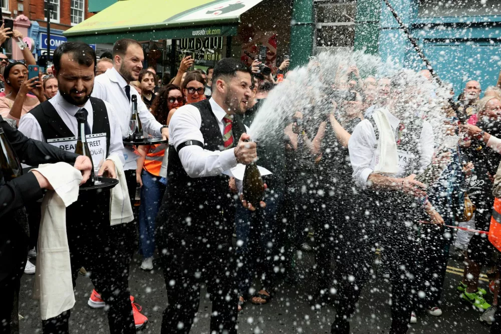 A server sprays champagne at the finish of the annual waiters' race during the 50th anniversary of the Soho Village Fete in London, Britain, July 20, 2025. REUTERS/Kevin Coombs