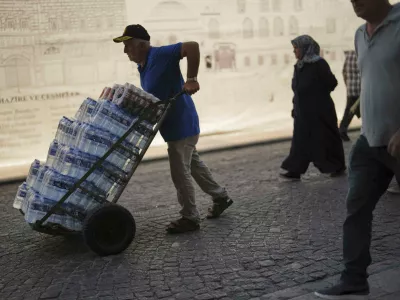 A man delivers plastic bottles of water to a local restaurant on a hot summer day at Eminonu district, in Istanbul, Turkey, Friday, July 25, 2025. (AP Photo/Francisco Seco)