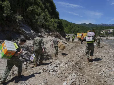 In this photo released by Xinhua News Agency, soldiers carry relief supplies for the trapped villagers by foot on a flood damaged road after heavy rains, in Miyun district on the outskirts of Beijing on Wednesday, July 30, 2025. (Ju Huanzong/Xinhua via AP)