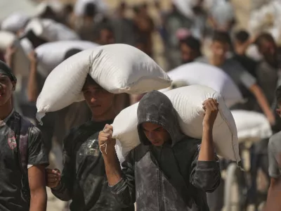 Palestinians carry sacks of flour taken from a humanitarian aid convoy en route to Gaza City, in the outskirts of Beit Lahiya, northern Gaza Strip, Friday, Aug. 1, 2025. (AP Photo/Jehad Alshrafi)