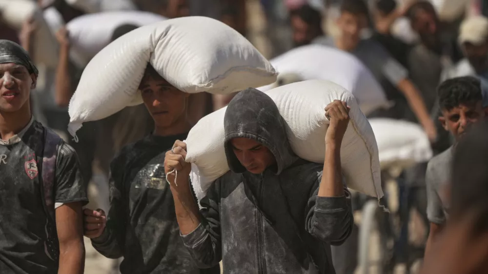 Palestinians carry sacks of flour taken from a humanitarian aid convoy en route to Gaza City, in the outskirts of Beit Lahiya, northern Gaza Strip, Friday, Aug. 1, 2025. (AP Photo/Jehad Alshrafi)