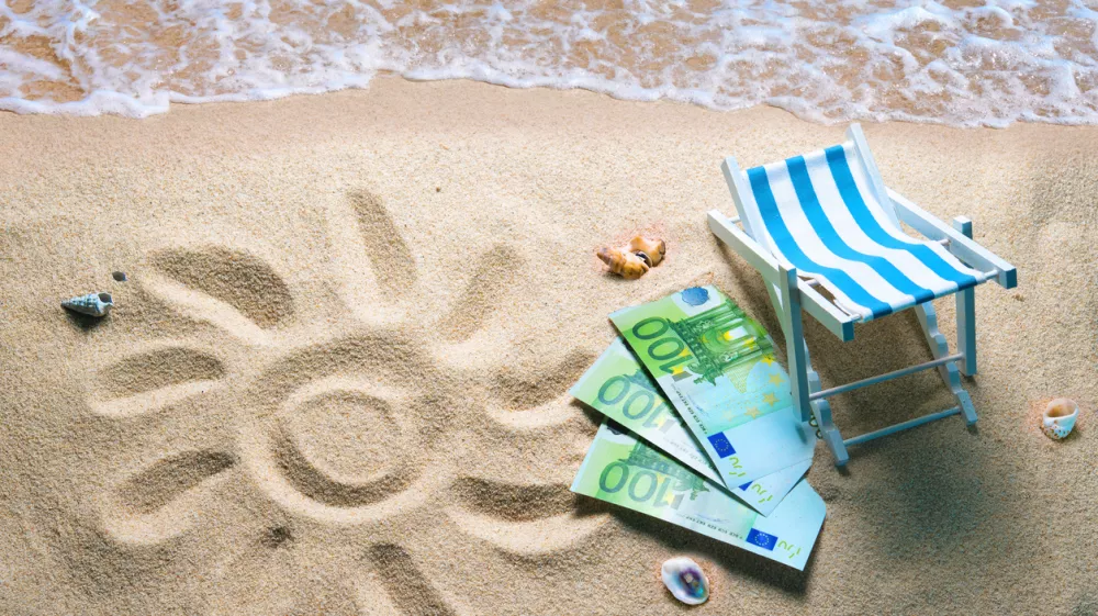 Deckchair with euro bills on a beach with a sun drawn on the sand. Travel money savings concept