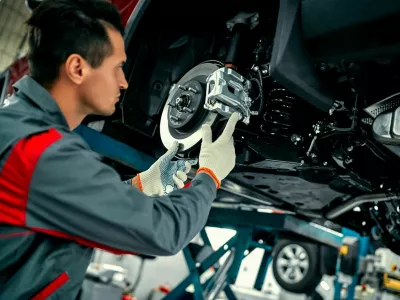 Car mechanic worker repairing suspension of lifted automobile at auto repair garage shop station