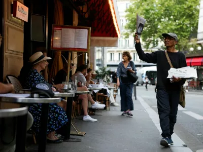 Ali Akbar, 73, known as the last newspaper hawker in the French capital sells 'Le Monde' newspaper to people on a terrace in the Latin Quarter, in Paris, France, August 4, 2025. REUTERS/Stephanie Lecocq / Foto: Stephanie Lecocq