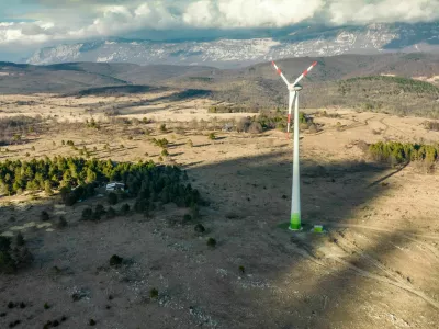 Wind turbine among ship pasture at winter sunset on Karst plateau. Behind is a mountain Nanos and village Dolenja vas.