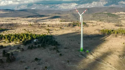 Wind turbine among ship pasture at winter sunset on Karst plateau. Behind is a mountain Nanos and village Dolenja vas.
