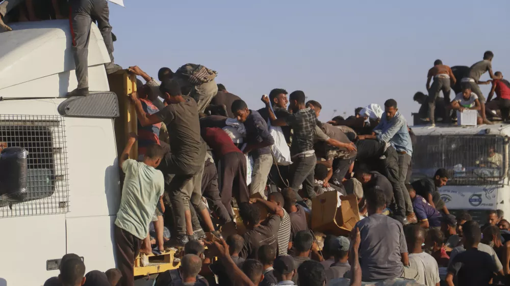 Palestinians struggle to get food and humanitarian aid from the back of a truck as it moves along the Morag corridor near Rafah, in the southern Gaza Strip, Monday, Aug. 4, 2025. (AP Photo/Mariam Dagga)