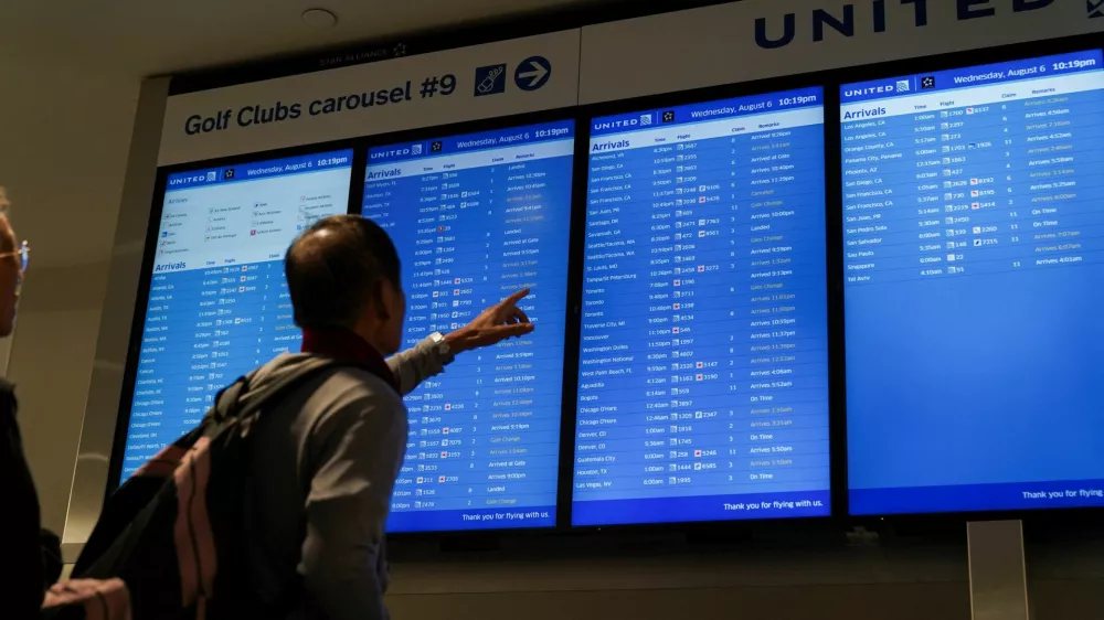 Travelers look upon a flight-arrival screen after United Airlines grounded flights due to a tech outage at Newark Liberty International Airport in Newark, New Jersey, U.S., August 6, 2025. REUTERS/Ryan Murphy