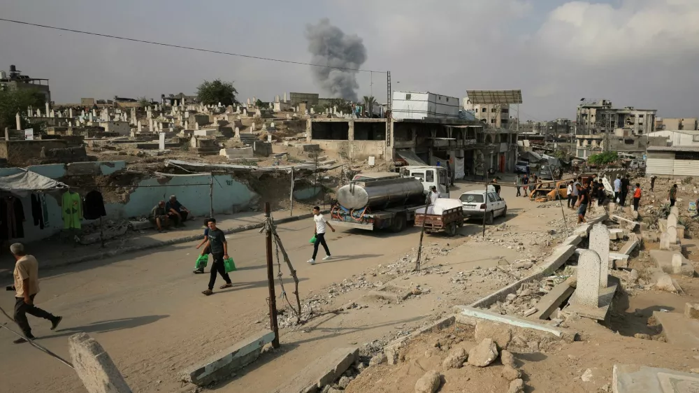 Palestinians walk past damaged graves as smoke rises following an Israeli strike, in Gaza City, August 13, 2025. REUTERS/Dawoud Abu Alkas