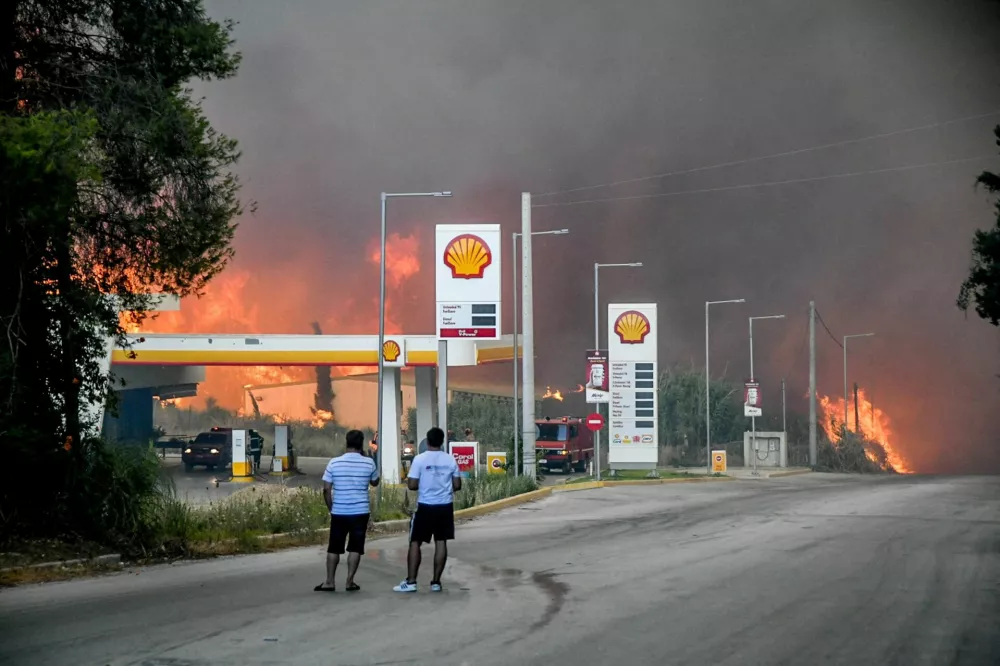 People watch as a wildfire burns near a gas station in Achaia, Greece, August 12, 2025. Eurokinissi via REUTERS ATTENTION EDITORS - THIS PICTURE WAS PROVIDED BY A THIRD PARTY. NO RESALES. NO ARCHIVES. GREECE OUT. NO COMMERCIAL OR EDITORIAL SALES IN GREECE