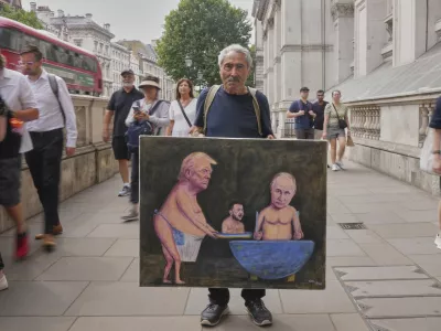 Satirical artist Kaya Mar, displays his latest painting depicting President Trump, Russian President Putin and Ukraine's President Zelenskyy, outside Downing Street, in London, Wednesday, Aug. 13, 2025. (AP Photo/Joanna Chan)