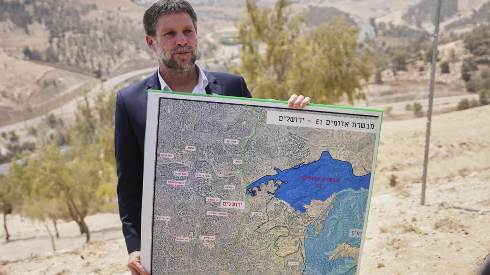 CORRECTS DAY Israeli Finance Minister Bezalel Smotrich holds a map that shows the E1 settlement project during a press conference near the settlement of Maale Adumim, in the Israeli-occupied West Bank, Thursday, Aug. 14, 2025. (AP Photo/Ohad Zwigenberg)