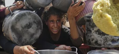 A Palestinian girl struggles to get donated food at a community kitchen in Gaza City, northern Gaza Strip, Saturday, Aug. 16, 2025. (AP Photo/Jehad Alshrafi)