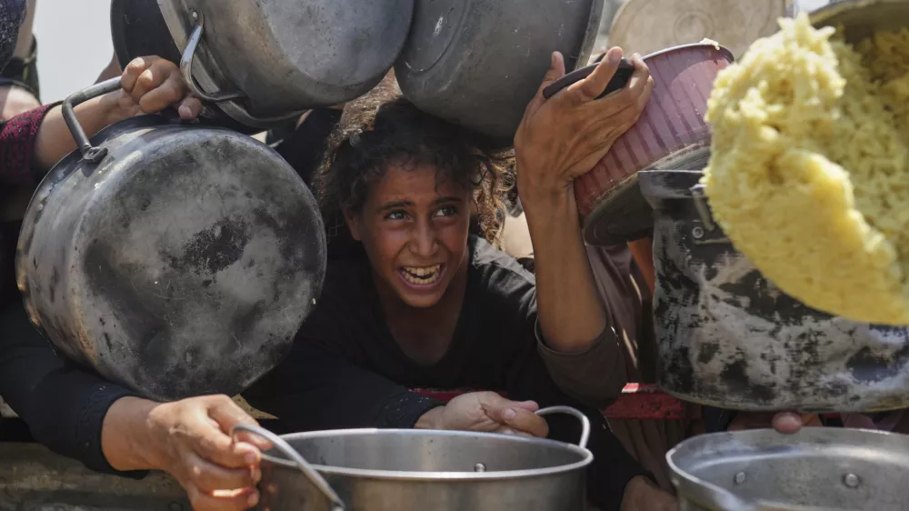 A Palestinian girl struggles to get donated food at a community kitchen in Gaza City, northern Gaza Strip, Saturday, Aug. 16, 2025. (AP Photo/Jehad Alshrafi)