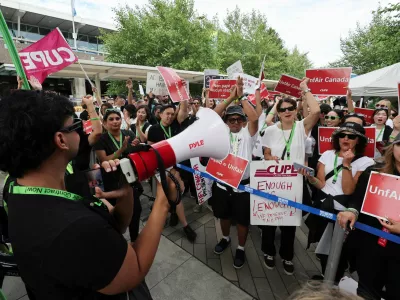 CUPE president Mark Hancock appears on a mobile phone screen as striking Air Canada flight attendants listen to a remote broadcast by megaphone by Hancock on the current situation, as they defy a back to work order at Vancouver International Airport in Richmond, British Columbia, Canada August 18, 2025. REUTERS/Chris Helgren