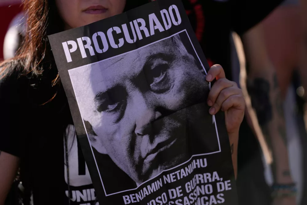 A demonstrator holds up a poster with an image of Israeli Prime Minister Benjamin Netanyahu, with "Wanted" written in Portuguese, during a protest at the US embassy against tariffs imposed by the American government and the US position in the Israel-Hamas war, in Brasilia, Brazil, Tuesday, Aug. 19, 2025. (AP Photo/Eraldo Peres)