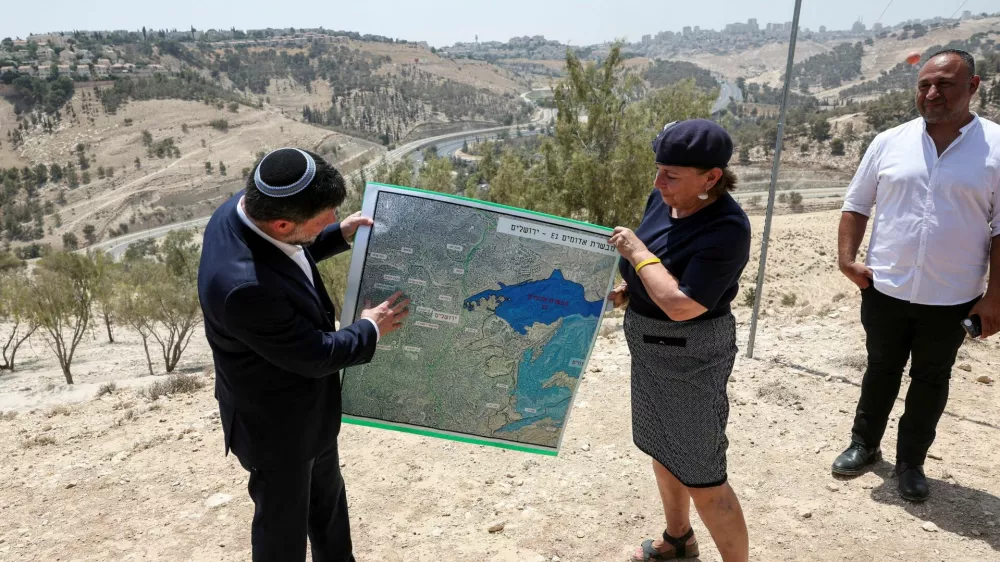 FILE PHOTO: Israeli Finance Minister Bezalel Smotrich and a woman hold a map that shows the long-frozen E1 settlement scheme, that would split East Jerusalem from the occupied West Bank, on the day of a press conference near the Israeli settlement of Maale Adumim, in the Israeli-occupied West Bank, August 14, 2025. REUTERS/Ronen Zvulun/File Photo
