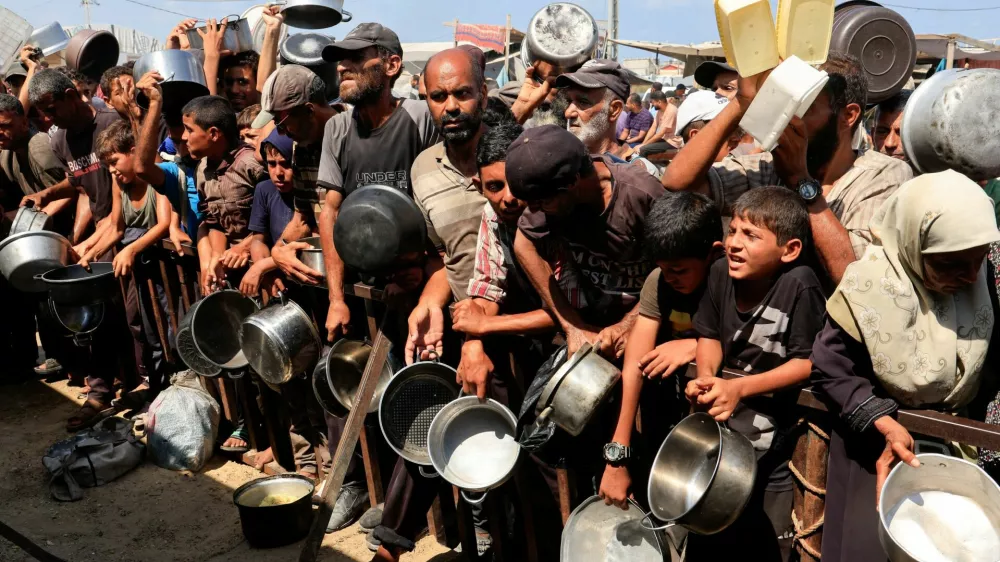 FILE PHOTO: Palestinians hold pots and containers while waiting to receive food from a charity kitchen in Khan Younis, southern Gaza Strip, August 21, 2025. REUTERS/Hatem Khaled/File Photo
