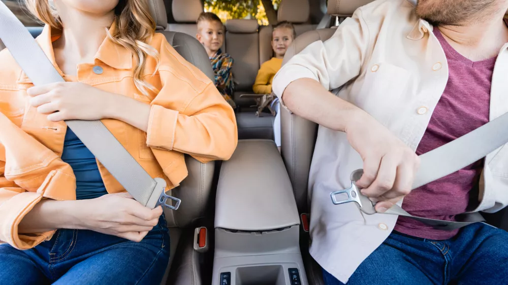 Smiling parents holding safety belts near kids on blurred background in car / Foto: Lightfieldstudios
