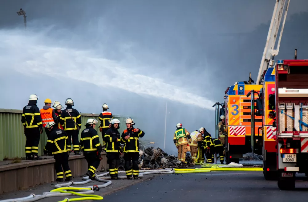 25 August 2025, Hamburg: Firefighters try to extinguish a fire in an industrial area in the port of Hamburg. A fire has broken out in a warehouse in the Port of Hamburg, causing a major motorway nearby to be closed. Photo: Daniel Bockwoldt/dpa