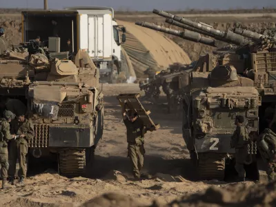 Israeli soldiers work on their armored vehicles parked in a staging area near the Israeli-Gaza border, as seen from southern Israel, Tuesday, Aug. 26, 2025. (AP Photo/Maya Levin)