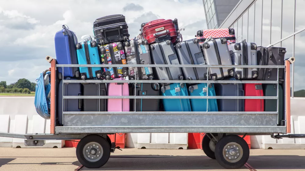 Trailer outside on airport filled with suitcases. When I arrived in Amsterdam on the airport Schiphol I took this image of packed suitcases on a standing trailer. Passengers on vacation take a lot of travel equipment or holiday gear with them. The trailer is parked outside, waiting to be transported to the plane or airplane.