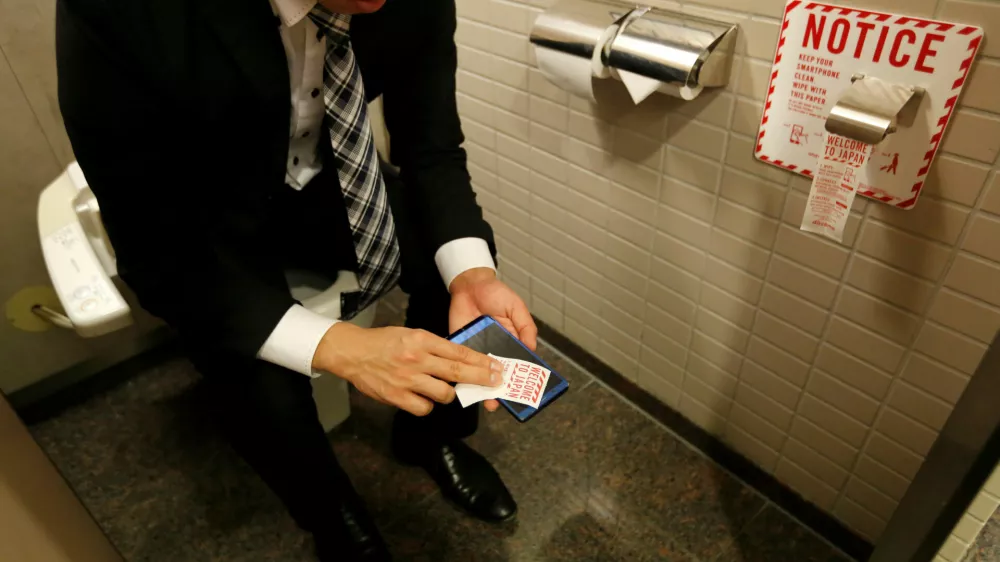 ﻿A man demonstrates a toilet roll for wiping smartphones, installed by Japanese mobile phone company NTT Docomo, in a high-tech bathroom equipped with bidet and heated seat at Narita international airport in Narita, Japan, December 28, 2016. REUTERS/Toru Hanai