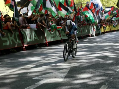 Cycling - Vuelta a Espana - Stage 18 - Valladolid to Valladolid - Valladolid, Spain - September 11, 2025 Israel - Premier Tech's Pier-Andre Cote in action as pro-Palestine protestors are pictured in the background REUTERS/Juan Medina
